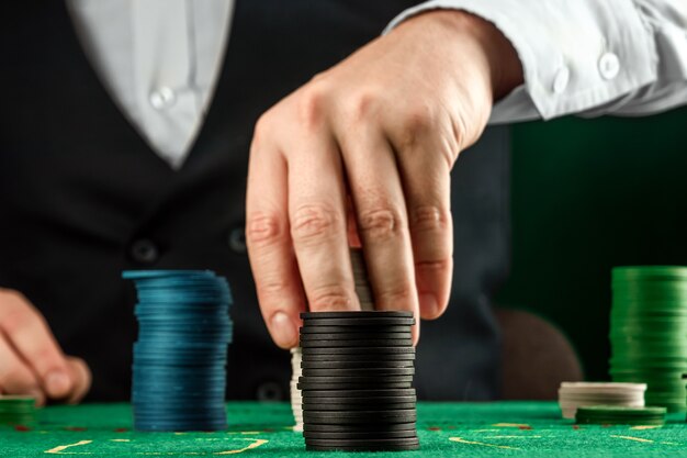 Мужские руки крупье в казино и игральные фишки на зеленой ткани крупным планом