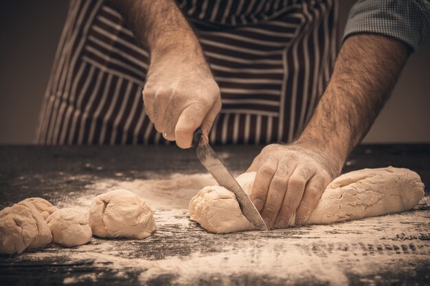 Мужские руки разрезают тесто. Шеф-повар готовит хлеб и булочку