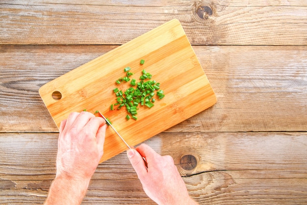 Male hands cut a green onion on a cutting board