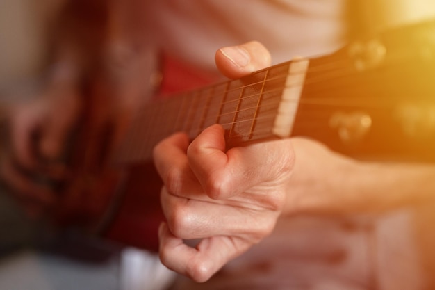 Male hands of an elderly senior caucasian man holding and playing a classical guitar close up at home unprofessional faceless guitarist people play amateur music domestic hobbies and leisure flare