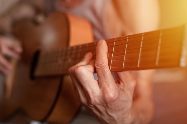 Male hands of an elderly senior caucasian man holding and playing a classical guitar close up at home unprofessional faceless guitarist people play amateur music domestic hobbies and leisure flare