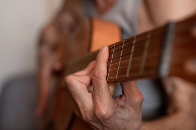 Male hands of an elderly senior caucasian man holding and\
playing a classical guitar close up at home unprofessional faceless\
guitarist people play amateur music domestic hobbies and\
leisure