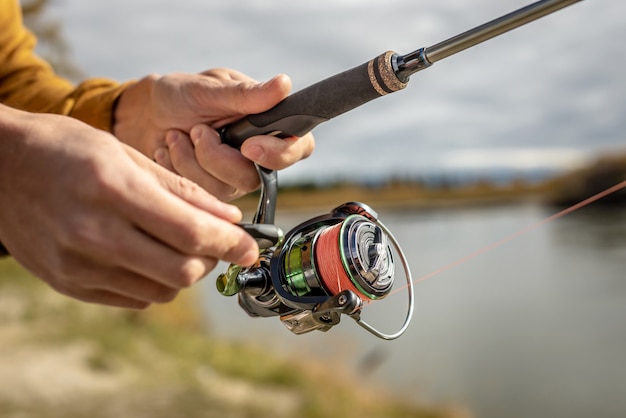 Male hands of a fisherman are holding a spinning closeup. Concept of fishing in the autumn forest