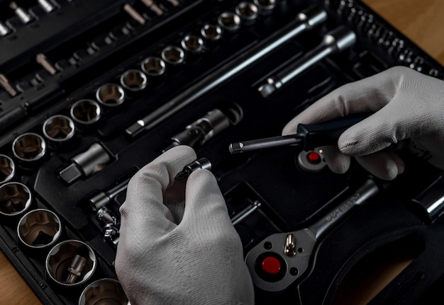 Male hands in gloves over open toolbox with different metal tools for car and home repair, close up.