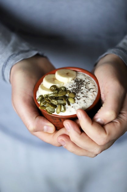 Male hands hold a bowl of yogurt. A man with a spoon eats yogurt with seeds. Chia pudding with pumpkin seeds and banana.