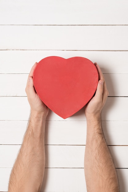 Male hands hold a red heart shaped box on a white wooden table