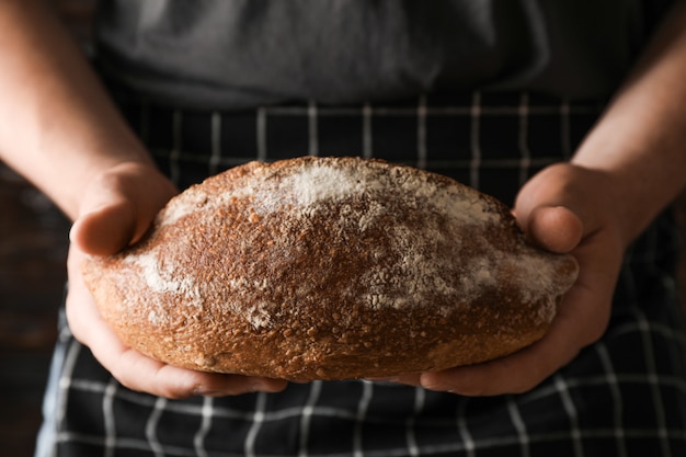 Male hands hold wheat bread against wooden space, space for text Male hands hold wheat bread against wooden space, space for text