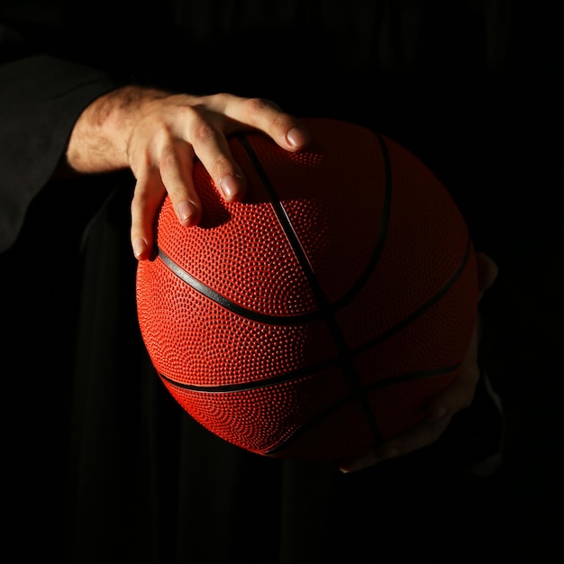 Мужские руки держат баскетбольный мяч на темном фоне