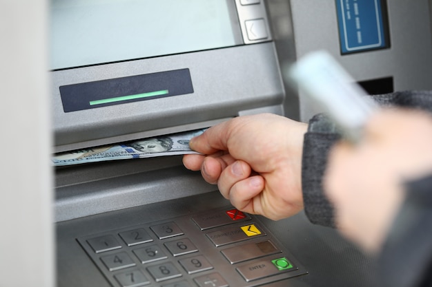 Male hands holding bunch of hundred dollars banknotes at atm machine