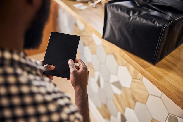 Mani maschili che tengono il pad elettronico del pc mentre l'uomo in piedi vicino al bancone con la borsa per la consegna del cibo