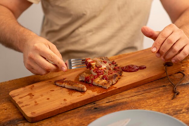 Male hands holding a fork with fried meat with ketchup on a wooden table