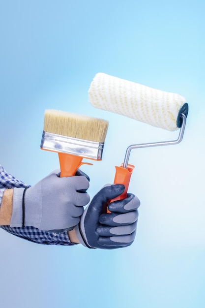 Male hands holding paint roller and brush decorating service