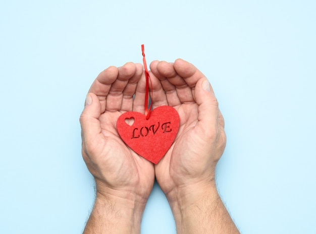 Male hands holding red heart on a blue