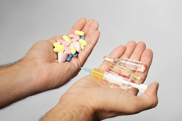 Male hands holding syringe and drugs on light background