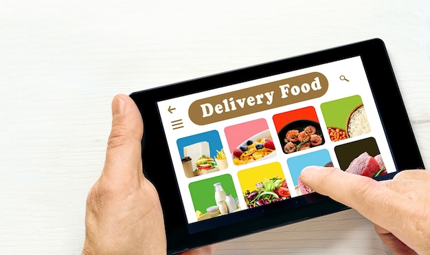 Male hands holding tablet computer with app delivery food on screen above white desk