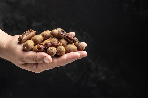 Male hands holding Tamarinds set beans in shell on a brown butchers block on a dark background Tropical healthy fruits banner menu recipe place for text