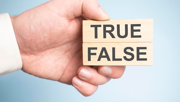 一方にTrue記号、もう一方にFalse記号が付いた2つの木製ペグを持っている男性の手。