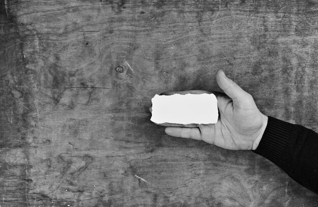 Male hands holding a white blank sheet of paper on the background of wooden texture table