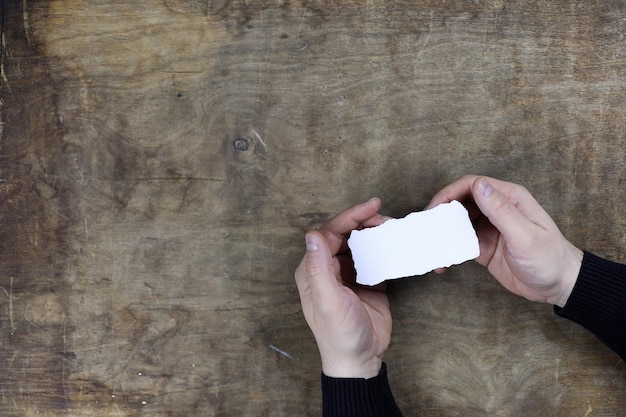 male hands holding a white blank sheet of paper on the background of wooden texture table
