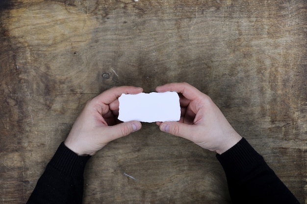 Mani maschili che tengono un foglio di carta bianco bianco sullo sfondo di un tavolo di struttura in legno