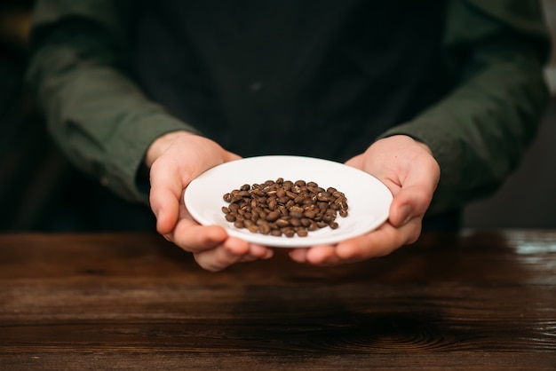 男性の手は、コーヒーの穀物と白いプレートを保持しています。