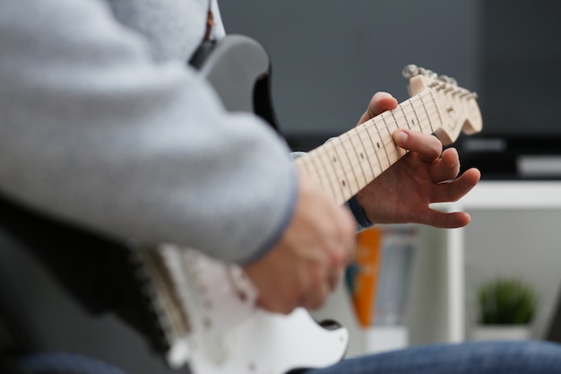 Male hands at home play and tune the electric guitar is engaged in music realizes listening enjoying music notation large concept closeup