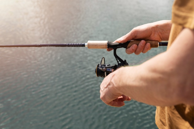 Male hands hoolding spinning rod, spoon-bait and fishing over blue water, close up.