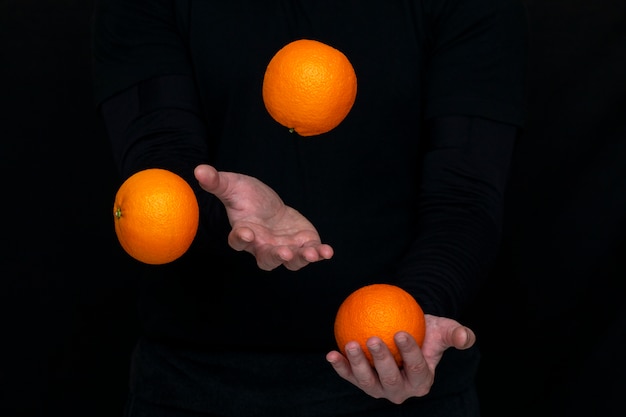 Photo male hands juggle with fresh oranges on a dark wall