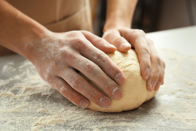 Male hands kneading dough on sprinkled with flour table, closeup