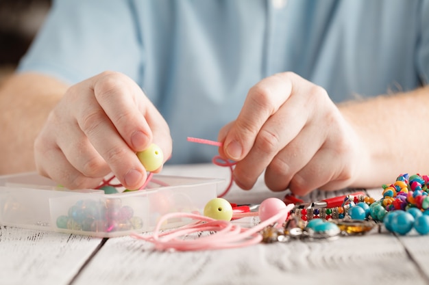 Male hands making a necklace with wooden beads