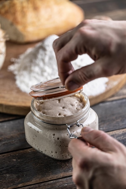 Male hands open a jar with active yeast flour and fresh bread and pastries in the background