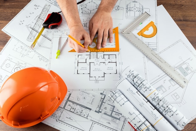 Male hands, Orange helmet, pencil, architectural construction drawings, tape measure