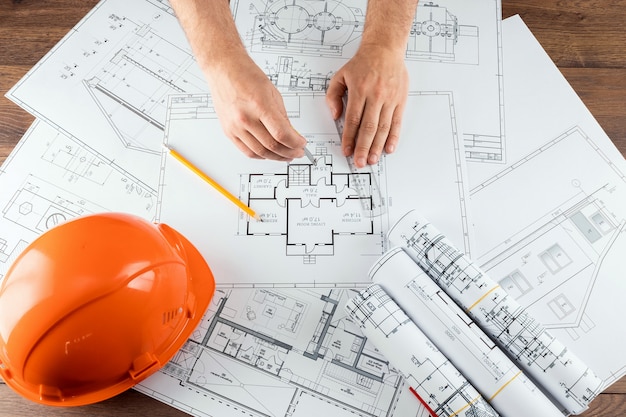 Male hands, Orange helmet, pencil, architectural construction drawings, tape measure.