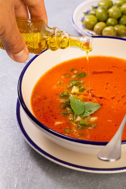 Male hands pour olive oil from a glass container into traditional Spanish gazpacho made of tomato, pepper, garlic with the addition of Tabasco sauce
