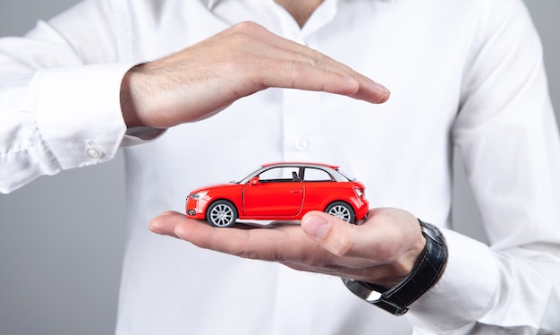 Male hands protect red toy car.