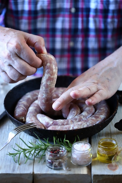 Male hands put raw sausages in a frying pan