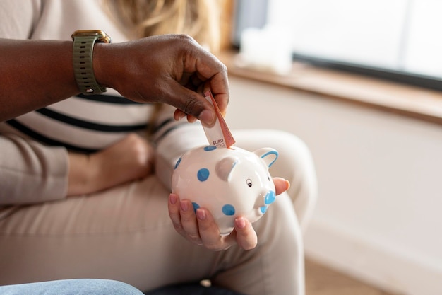 Male hands putting money in piggy bank while woman holding it at home