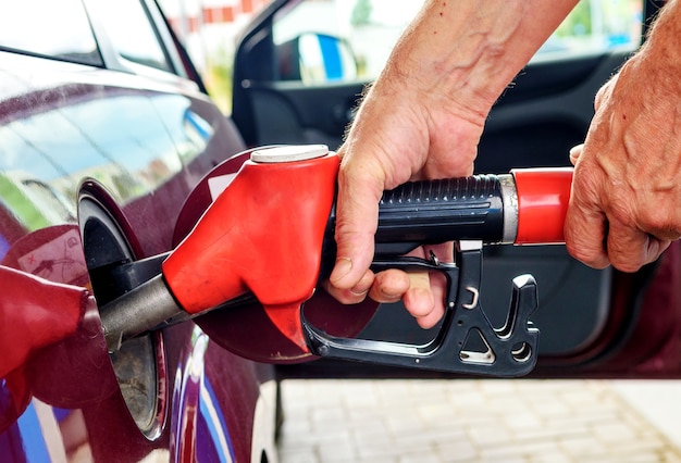 Foto le mani maschili che fanno rifornimento di carburante a un'autovettura tengono una pompa del carburante rossa.