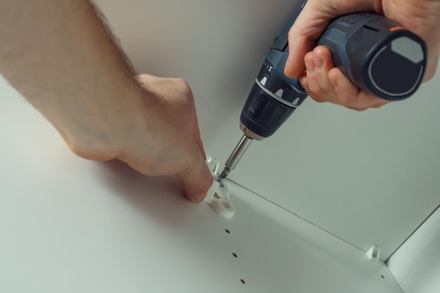 Male hands screw in to insert plastic support into one of series of holes to fix white hanger bar Holds screwdriver