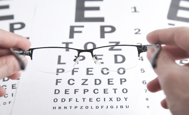 Male hands showing eyeglasses. Eye test chart.