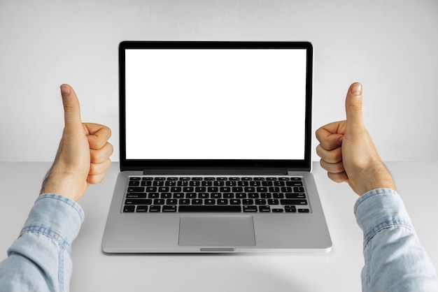 Mani maschii che mostrano i pollici in su e computer portatile con schermo bianco vuoto