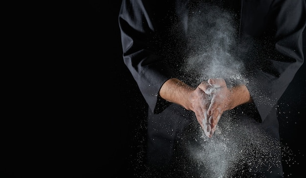 Male hands and splash of white wheat flour on a black background