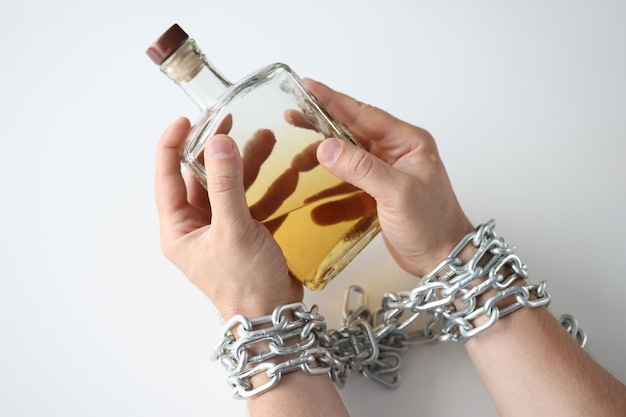 Male hands tied with chain and hold bottle of alcohol addiction and alcoholism concept