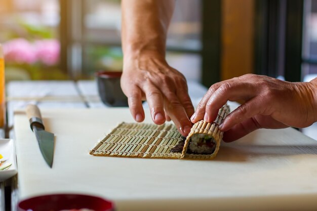 男性の手が竹マットに触れます。小さな竹マットの横にあるナイフ。寿司の作り方。料理の先生の丁寧な手。