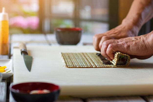 Male hands touching bamboo mat. Small bamboo mat and knife. Experienced sushi chef. Preparing healthy meal with seafood.