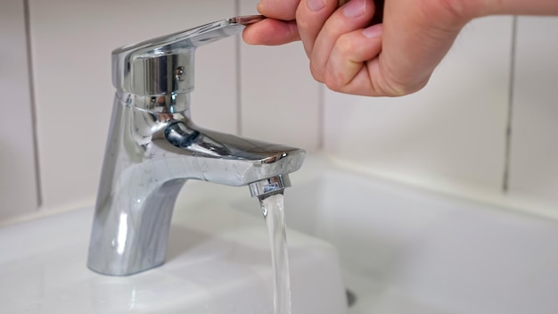 Male hands turn on water faucet and water quickly flows