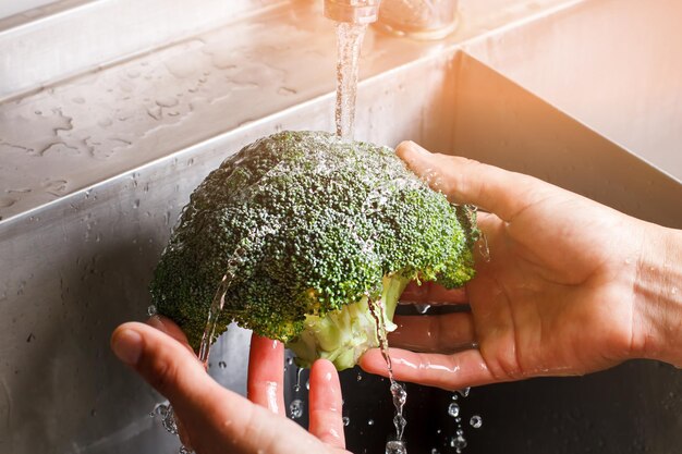 Male hands washing broccoli.