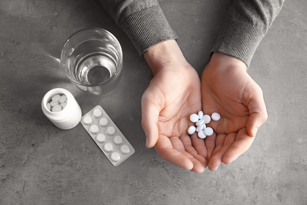 Male hands with pills and glass of water on grey textured background