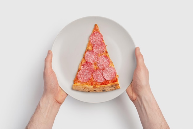 ナイフとフォークで白い背景に灰色のプレートにピザのスライスを持つ男性の手