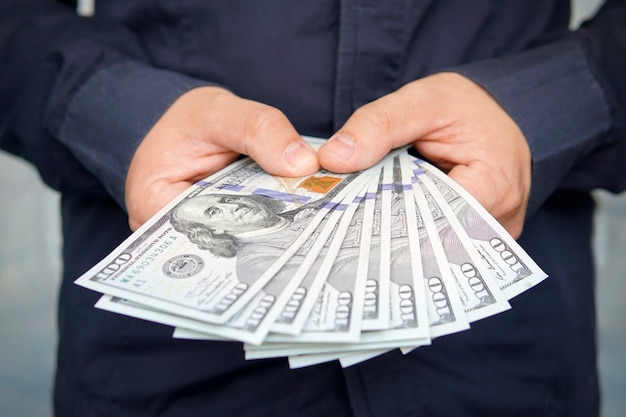 Male hands with wrist watch is considered American dollars. Hands holding dollar cash. 1000 dollars in 100 bills in a man hand close-up on a dark background. hundred